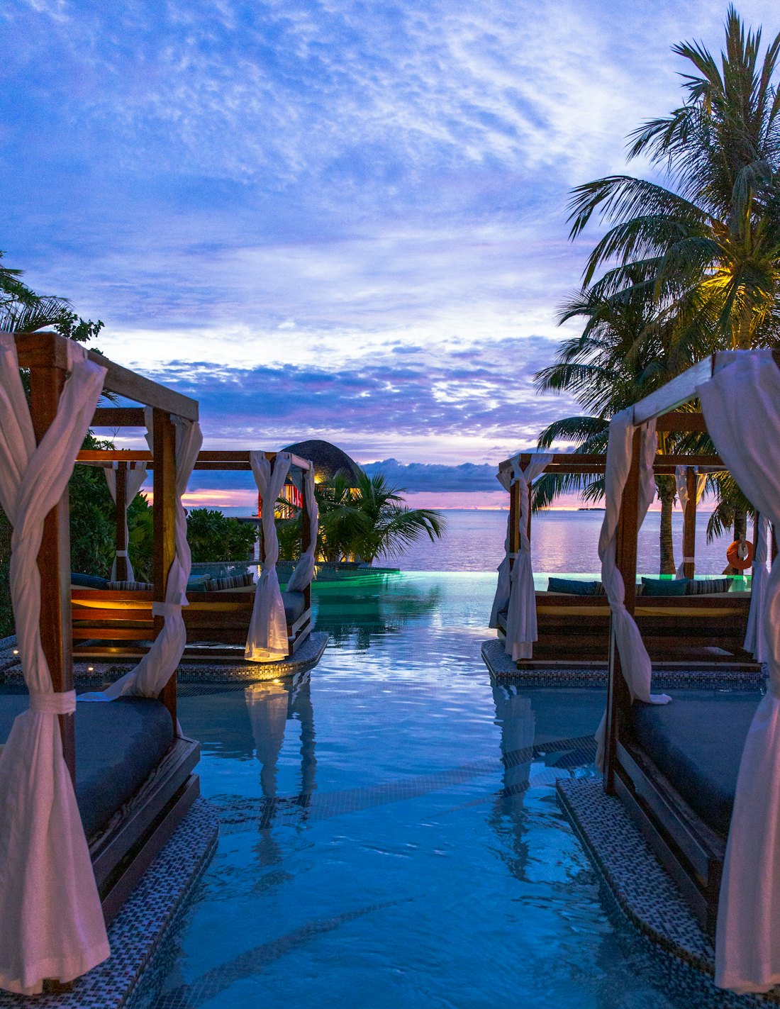 Candle-lit cabanas beside an infinity pool at sunset